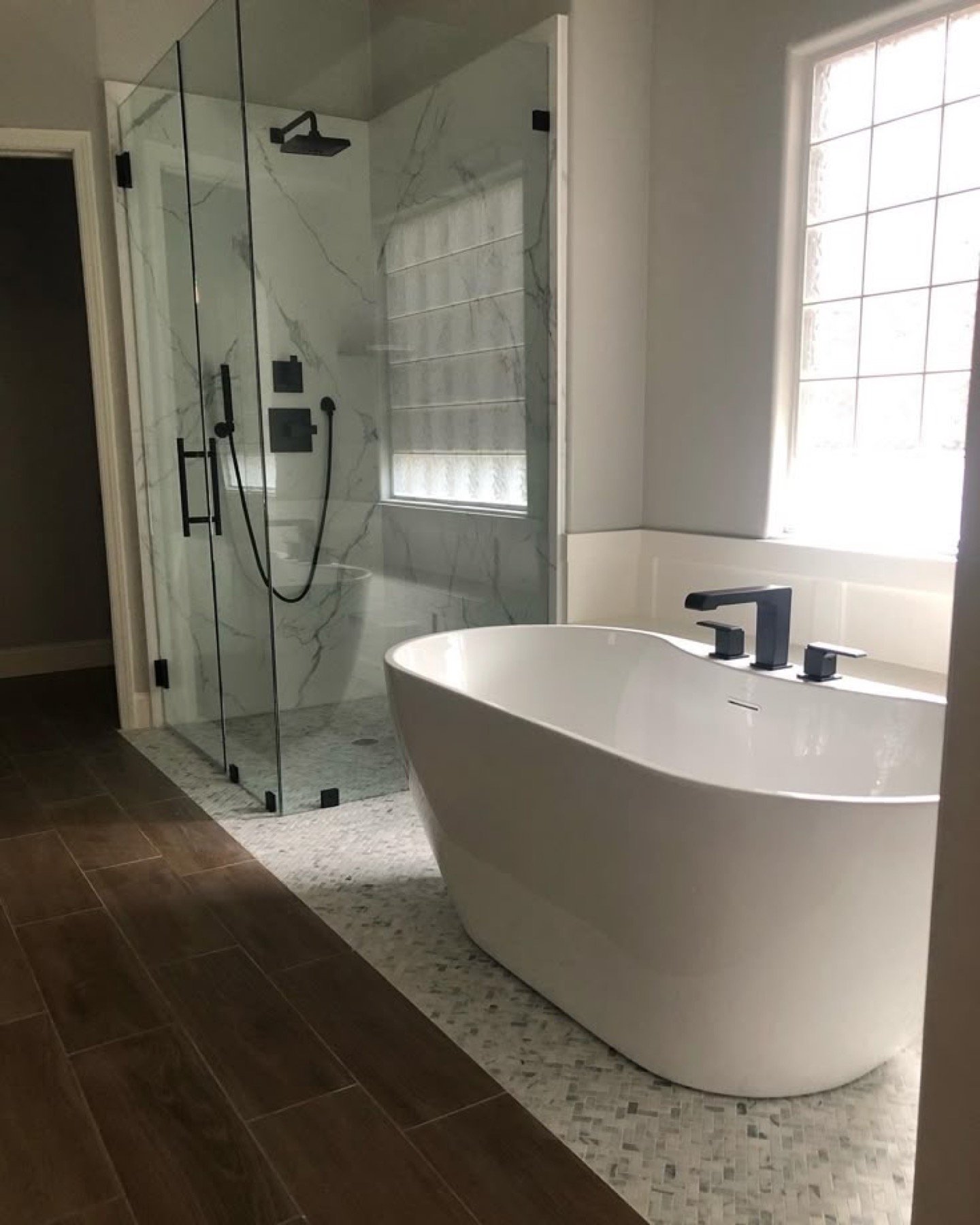 Marble-look walk-in shower beside a freestanding tub